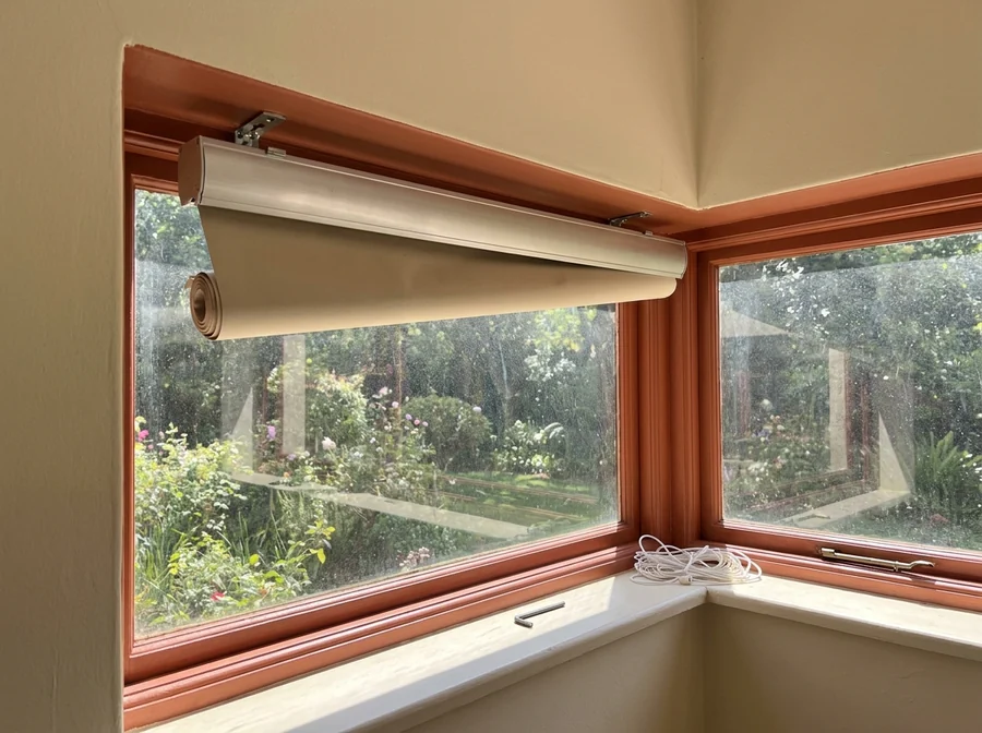 A roller blind headrail still in its brackets above a Melrose corner window, tube part-unrolled and a fresh cord coil on the sill during a repair
